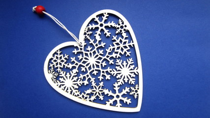 Cut out in wood a white ornamental heart on a string with a red bead on a blue background. Flat lay.  Creative Christmas gift idea