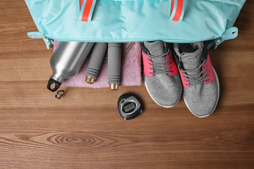 Open sports bag with gym stuff on wooden background, flat lay