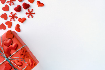 Festive composition from tied red gift box, snowflakes and hearts scattered on white background, valentines day concept