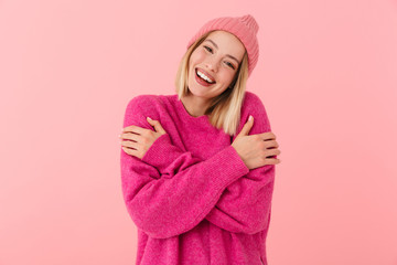Image of blonde girl wearing warm sweater smiling and hugging herself