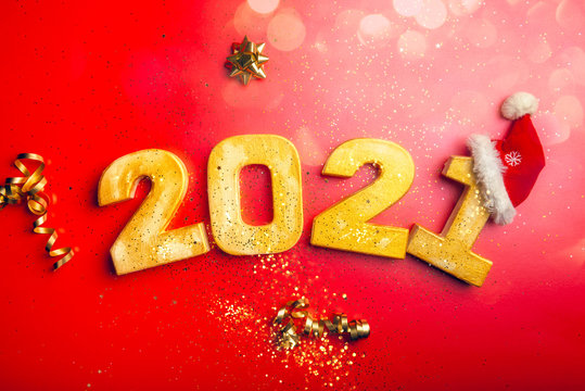 Happy New Year 2021. Golden digits 2021 with christmas hat are on red background with glitter. Holiday Party Decoration or postcard concept with top view and copy space.