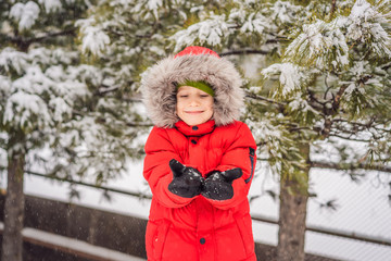 Happy boy plays with snow. Cute kid throwing snow in a winter park. Happy winter holidays. Winter fashion