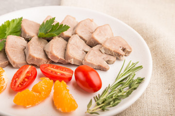 Boiled pork tongue with tomatoes and herbs on a gray concrete background. Side view, selective focus.