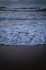 Water foam on the seashore of Zurriola Beach after sunset