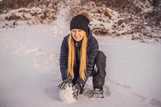 Young woman rolling giant snowball to make snowman