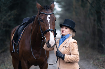 A 50 year old woman rides a horse. Walking with a horse. He is engaged in hippotherapy. A woman is wearing a trendy derby costume.
