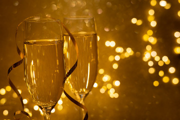 Two glasses of champagne on golden glittering background with defocused lights. Christmas and New Year holidays concept. Copy space. Soft focus