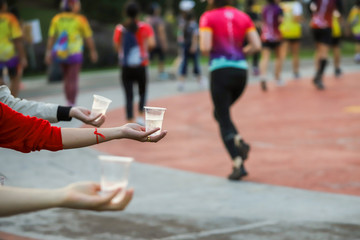 Hand of a volunteer giving a cup of water at a refreshment point in a marathon race to runners.,...