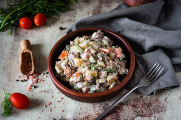 Meat salad Olivier with peas, vegetables and mayonnaise on a clay plate on a gray background