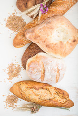 Different kinds of fresh baked bread on a white wooden background. top view.