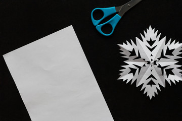 Sheet of paper, snowflake, scissors on the black background