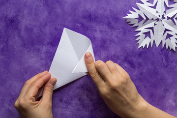 Woman hands folding triangle sheet of paper in half to make smaller triangle on the violet surface