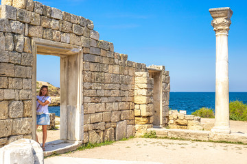 girl stands at the stone wall of the ancient city of Khersones on the seashore