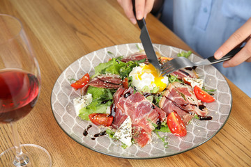 Woman eating delicious prosciutto salad with vegetables at wooden table, closeup