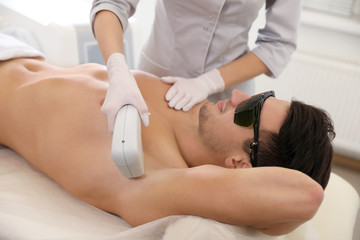 Obraz na płótnie Canvas Young man undergoing laser epilation procedure in beauty salon