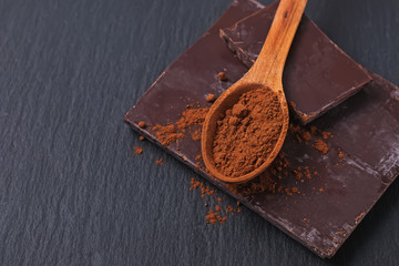 Bar of natural chocolate and cocoa powder in a wooden spoon close-up