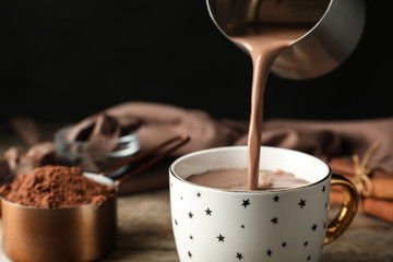 Pouring hot cocoa drink into cup on wooden table