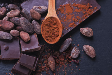 Natural chocolate and cocoa powder in a wooden spoon on black stone bacgkround