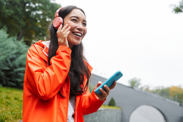 Smiling young asian woman wearing raincoat walking outdoors