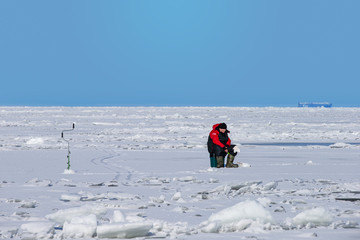 Fototapeta na wymiar Man ice fishing on a frozen Gulf of Finland
