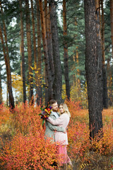 Couple in love walks through autumn forest. Hugs and kisses of men and women, relationships and love. Young couple stands in yellow red grass, a bouquet of flowers in girl hand