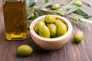 Green olives and olive oil in bottle on the wooden table