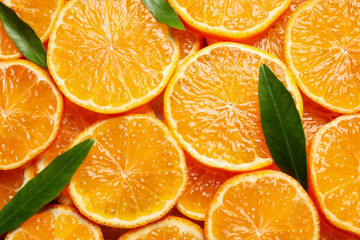 Slices of fresh ripe tangerines and leaves as background, top view. Citrus fruit