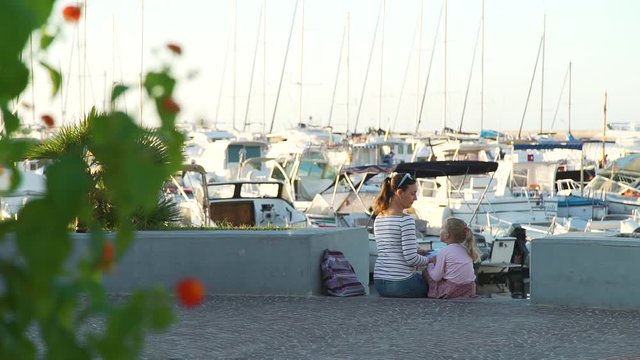 Young Woman Tourist Talking with her Little Daughter while Sitting near Yachts and Boats Parking in Forio Town on Ischia Island, Italy. Slow Motion. Family Holidays, Vacation and People Concept