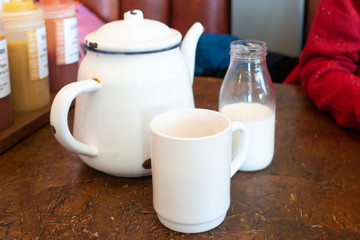 Teapot, cup and milk on a wooden table.
