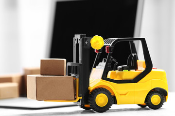 Toy forklift with boxes near laptop on table. Logistics and wholesale concept