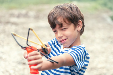 A boy in a striped T-shirt shoots a slingshot, front view. concept of naughty boy