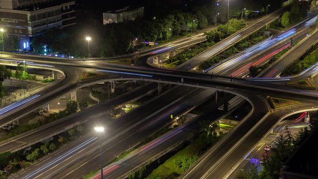 Timelapse flashing automobile silhouettes on wide Chengdu highways and overpass roads interchange by trees in China Sichuan province at dark night
