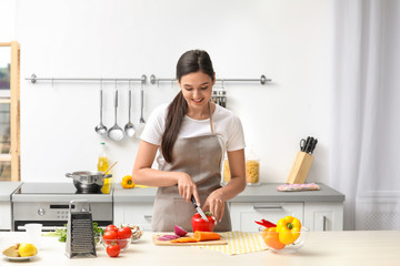 Young woman cutting vegetables for soup at table in kitchen