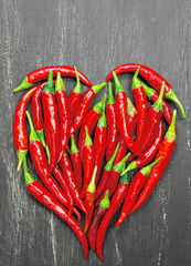 Hot peppers forming a heart on old wooden table black
