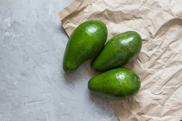 Three ripe avocados with a bone on a gray background and paper. half an avocado. The view from the top. Flat composition. The concept of the summer food. Vitamins from foods. space for text.