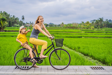 Obraz premium Mother and son ride a bicycle on a rice field in Ubud, Bali. Travel to Bali with kids concept