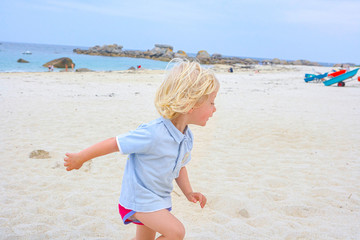 Happy cute active little boy playing in the sand at a beach in Brittany