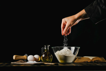 Dough preparation process. Chef adds ingredients to flour on a black background.
