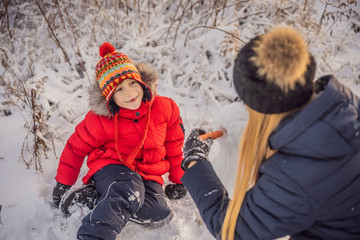 Happy family in warm clothing. Smiling mother and son making a snowman outdoor. The concept of winter activities