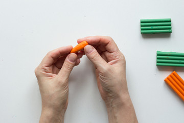 Woman hands making small carrot polymer clay on white background