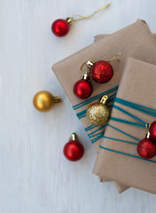 Three gifts wrapped in craft paper with bright red and gold Christmas balls in the form of balls. 