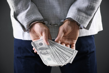 Man in handcuffs holding bribe money on dark background, closeup