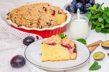 Pie with plums and shtreisel on a plate on a white wooden background. Rustic style. Homemade baking.