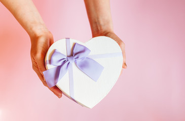 Hands of a lady holding gift box on a pastel background for Valentine's Day