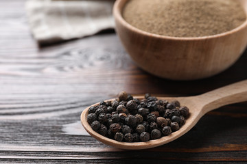 Peppercorns in spoon on wooden table, closeup