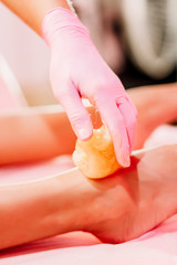 Close-up hands of cosmetologist in rose gloves applying paste for sugaring depilation. A master makes removing unnecessary hair on the legs. Procedure removal in a beauty salon. Depilatory sugar paste