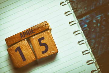 april 15th. Day 15 of month,Handmade wood cube with date month and day placed on a lined notebook on a blue background. artistic coloring.  spring month, day of the year concept