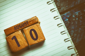 august 10th. Day 10 of month,Handmade wood cube with date month and day placed on a lined notebook on a blue background. artistic coloring.  summer month, day of the year concept