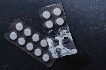 Two used blisters with white tablets on a black background. Drugs and medicine addiction
