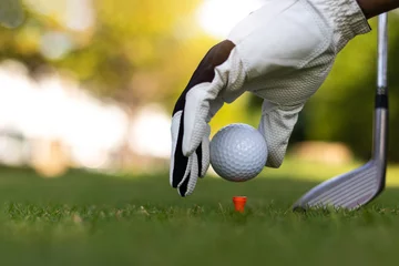 Schilderijen op glas Golf ball on green grass field. sport golf club,Hand hold golf ball with tee on golf course © poylock19